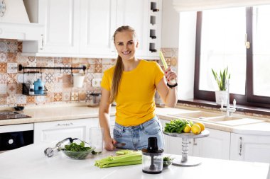 Güzel, narin bir kadın mutfakta sebze doğruyor ve yeşil meyve püresi için malzemeleri hazırlıyor. Sağlıklı yaşam tarzı, çevre dostu yiyecekler, diyet, vejetaryenlik