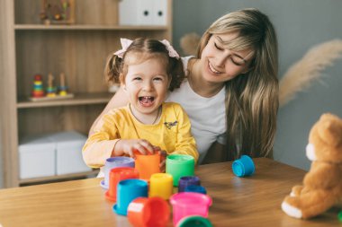 Annem ve gülen küçük bir kız evdeki masada renkli kalıplarla oynuyorlar. Birlikte zaman geçirmek, annelik, ebeveynlik.