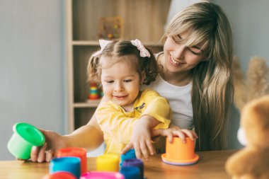 Annem ve gülen küçük bir kız evdeki masada renkli kalıplarla oynuyorlar. Birlikte zaman geçirmek, annelik, ebeveynlik.