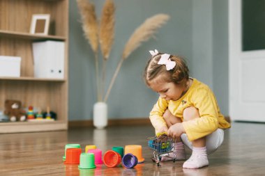 Güzel küçük bir kız oyuncak kalıplarıyla oynar ve bir evin ya da anaokulunun zeminine piramit inşa eder. Çocukluk, oyuncaklar, mutlu zamanlar