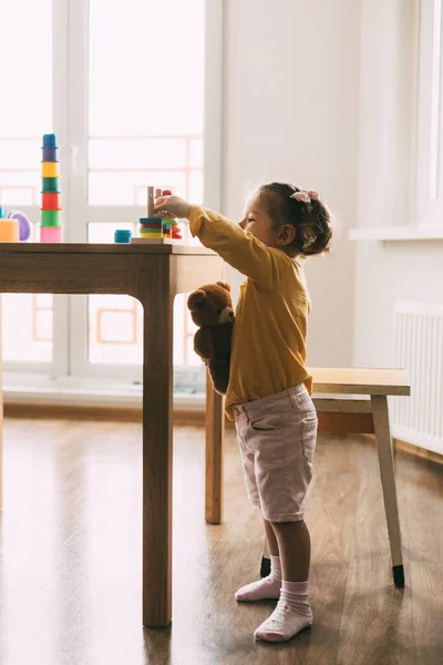 A little girl sorts colorful geometric shapes. Development of motor skills. Development of motor skills and styling of figures.