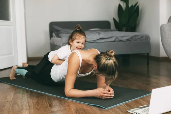 A young sports mom and a girl together do exercises at home. Healthy development of parents and children, healthy lifestyle