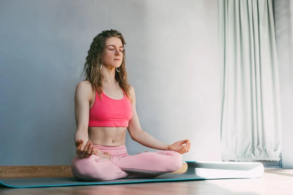 Uma bela jovem com os olhos fechados medita na posição de lótus na sala de aula.Esportes, fitness, ioga. Espaço para texto — Fotografia de Stock