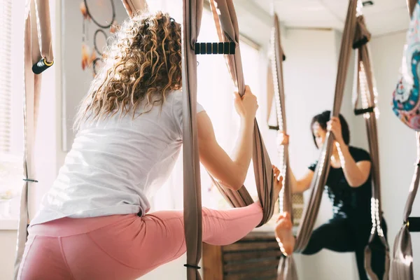 Una ragazza con i capelli ricci pratica yoga con un'amaca. Yoga, aero yoga, fitness, stile di vita. Vista posteriore — Foto Stock