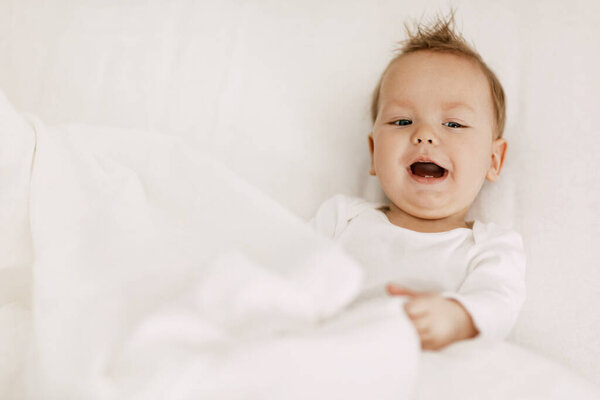The kid lies in a snow-white bed under the covers, laughs and indulges