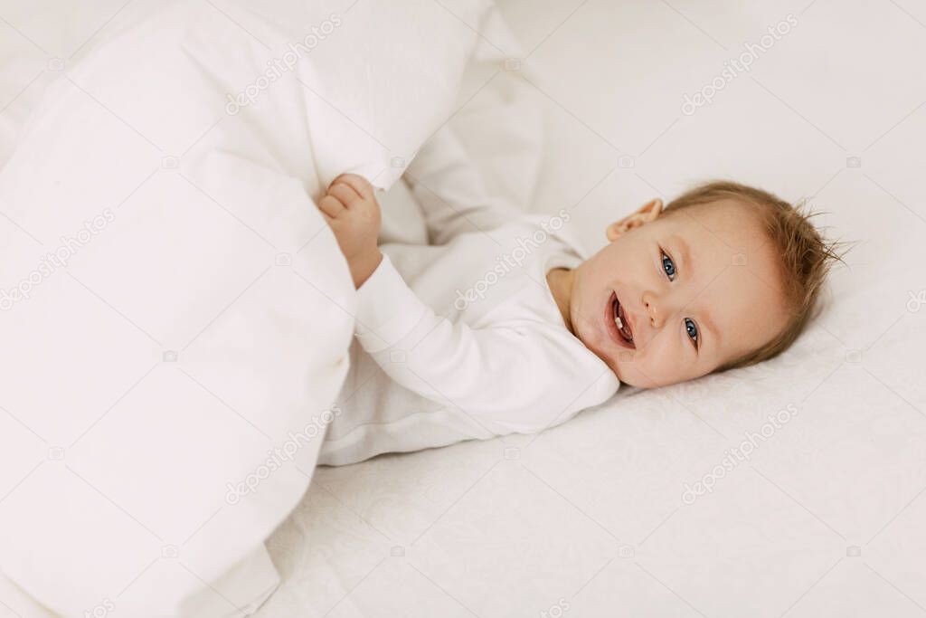 The kid lies in a snow-white bed under the covers, laughs and indulges