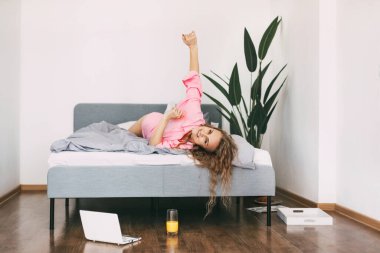 Güzel sarışın kadın sabah uyanıp hafta sonunun tadını çıkardıktan sonra yatakta meyve suyu içer.