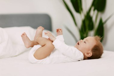 Çocuk kar beyazı bir yatakta yorganın altında yatıyor, gülüyor ve şımartıyor.