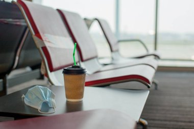 Boş bir havaalanındaki masada koruyucu bir maske ve bir fincan kahve var. Coronavirus, sosyal uzaklık, tecrit