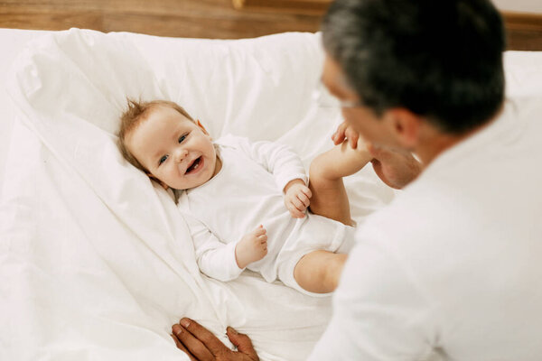 Счастливый отец играет с очаровательным ребенком в спальне на белоснежной кровати