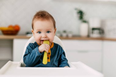 Bebek, mutfakta sarı bir kaşıkla yüksek bir sandalyede oturuyor.