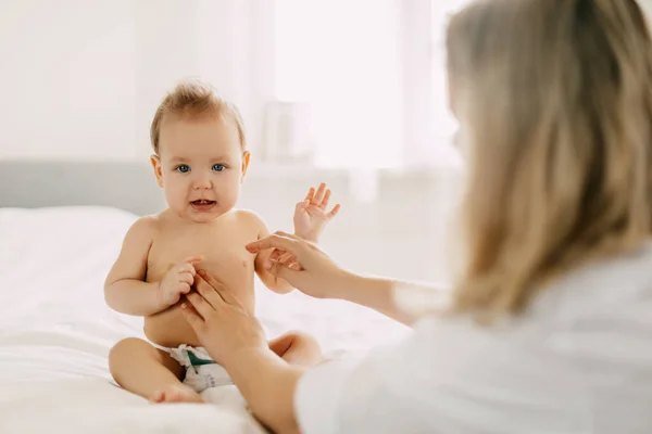 A young mother smears the babys tummy with baby cream. Child care, childhood, parenting — Stock Photo, Image