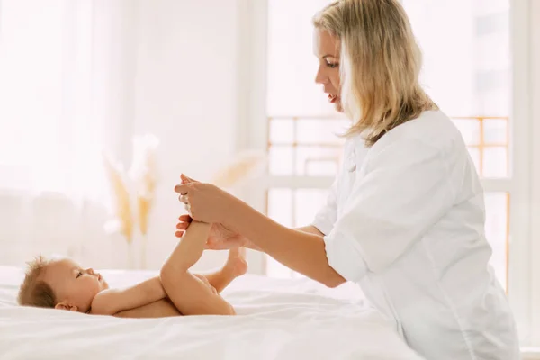 En ung mor masserar försiktigt sina barnben. Barnomsorg, barndom, moderskap — Stockfoto