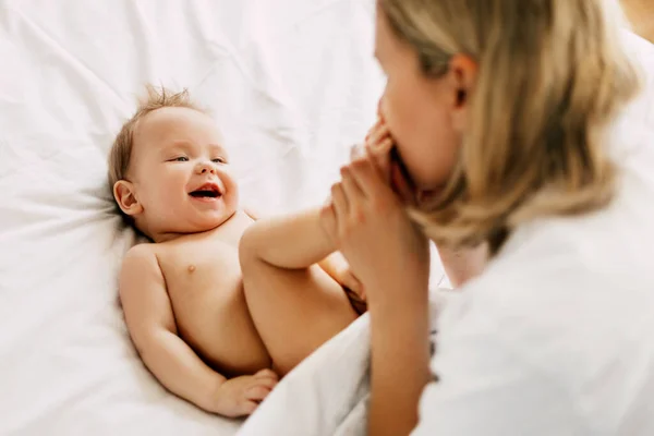 Lycklig mamma leker med sitt leende barn, kysser hans små fötter. Omsorg, kärlek, barndom, moderskap — Stockfoto