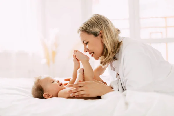 Mamma gioca con il suo bambino allegro e gli sorride. Cura, amore, infanzia, maternità. Vista laterale, spazio per il testo — Foto Stock