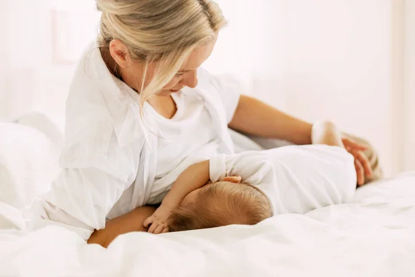 En ung mamma ammar sitt nyfödda barn medan hon ligger på sängen. Vård, barndom, moderskap — Stockfoto