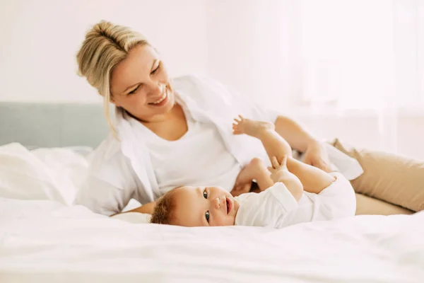 Lycklig mamma leker med sin lille son liggande på sängen, mamma och barnet kopplar av tillsammans. Oskuld, enhet och familj — Stockfoto