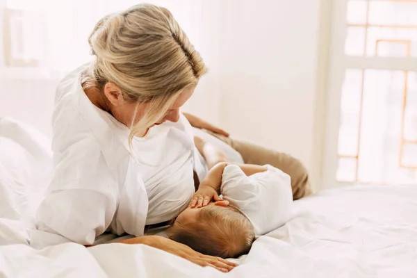 En ung mamma ammar sitt nyfödda barn medan hon ligger på sängen. Vård, barndom, moderskap — Stockfoto