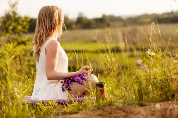 A young girl meditates in nature, a bouquet of lupines on her lap. Side view, space for text — Stock Photo, Image