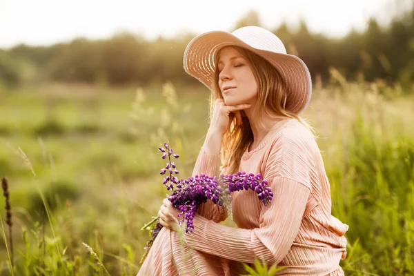 Portrait of a beautiful blonde with a bouquet of lupines in her hands sitting on the lawn — Stock Photo, Image