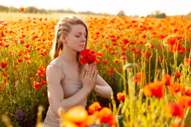 Kapalı gözlü güzel bir kız elinde bir buket çiçekle gelincik tarlasında meditasyon yapıyor.