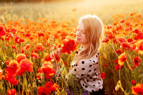 한 젊은 여인 이 노을에 양귀비 밭에 앉아 붉은 양귀비 꽃다발을 들고 있다 — 스톡 사진