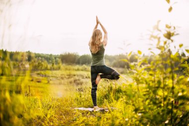 Genç bir kadın açık havada yoga yapıyor. Arka görünüm, metin için boşluk. Yoga, fitness, spor