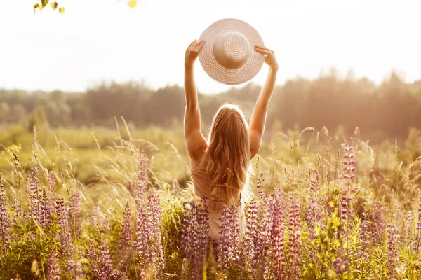 밝은 옷을 입은 한 소녀가 뻗친 팔에 모자를 쓰고 소나무밭을 바라보며 석양을 바라보고 있다. 왼쪽시야, 본문을 위한 공간 — 스톡 사진