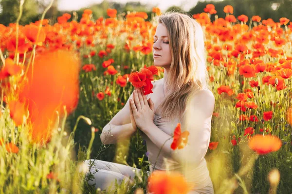 Uma menina bonita com olhos fechados medita em um campo de papoula segurando um buquê de flores — Fotografia de Stock