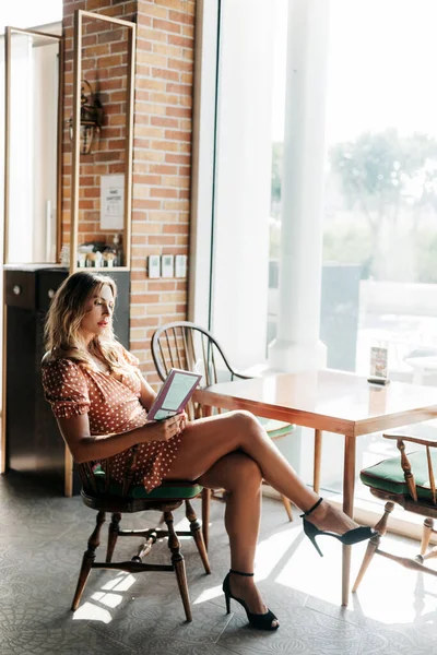 Uma bela jovem lê um livro sentado a uma mesa em um café moderno — Fotografia de Stock