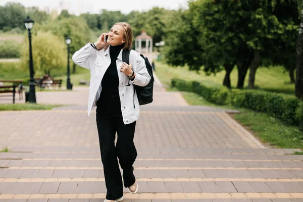 Rubia feliz caminando en un parque de la ciudad, hablando por teléfono — Foto de Stock