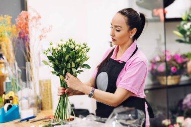 Güzel bir çiçekçi kadın çiçekçisinde çiçeklerden bir kompozisyon yapar. Bir buket çiçek, hediye, selam