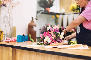 Çiçekçi bir kızın hediye kağıdına sardığı güzel bir buket çiçeğin yakın çekimi. Çiçek işi, çiçeklerle çalışmak, çiçek buketi.
