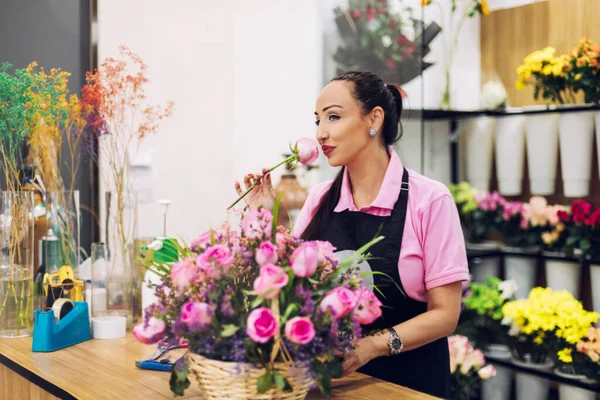A florist girl holds a rose in her hand and inhales its fragrance before making a bouquet