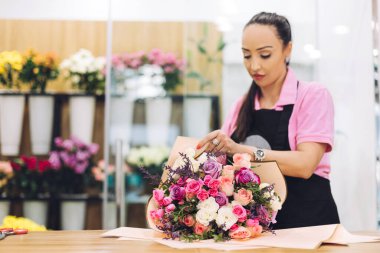 Çiçekçi bir kızın hediye kağıdına sardığı güzel bir buket çiçeğin yakın çekimi. Çiçek işi, çiçeklerle çalışmak, çiçek buketi.