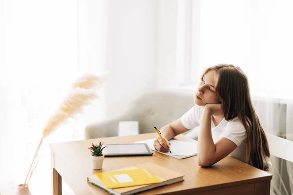 Una adolescente mira pensativamente a la distancia mientras hace su tarea sola. El concepto de enseñanza y educación, deberes —  Fotos de Stock