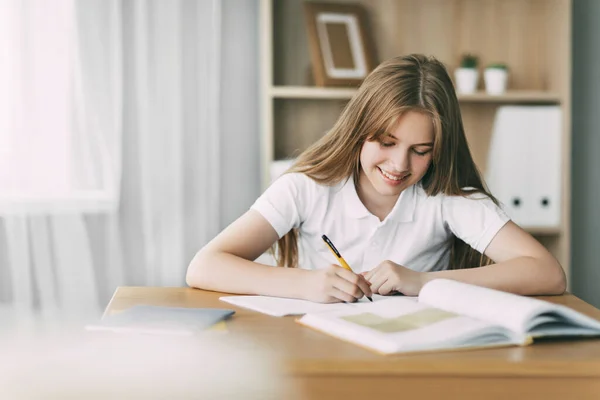 Una chica sonriente hace su tarea, escribe una sinopsis, y se prepara para las conferencias. Concepto de formación y educación — Foto de Stock