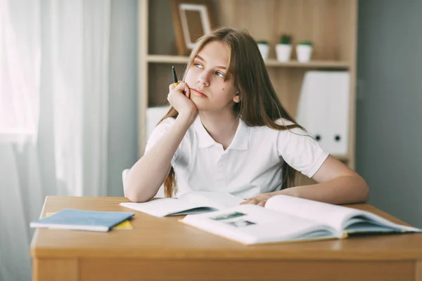 Una adolescente mira pensativamente a la distancia mientras hace su tarea sola. El concepto de enseñanza y educación, deberes — Foto de Stock