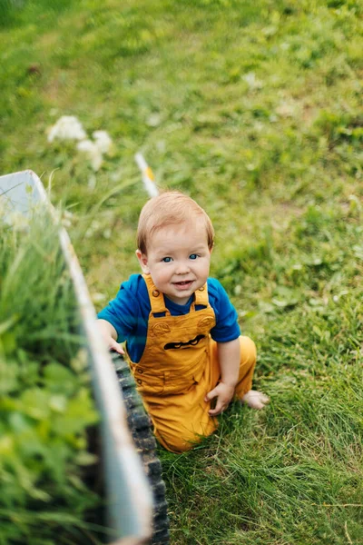 Kind sitzt auf dem Gras neben einem Gartenwagen und lächelt — Stockfoto