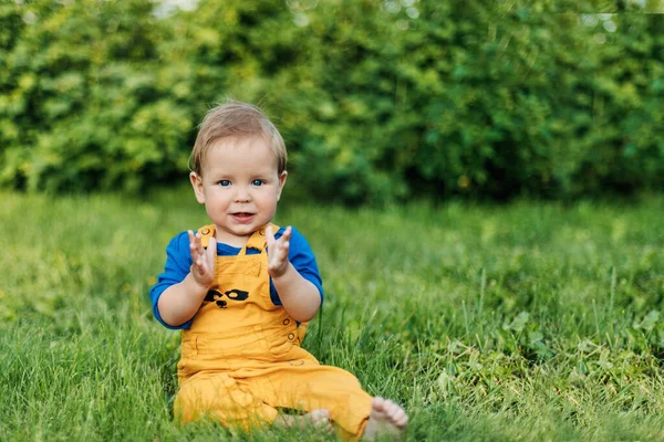 Glücklicher, charmanter Junge in modischen Klamotten, der an einem Sommertag auf dem Rasen im Garten sitzt — Stockfoto