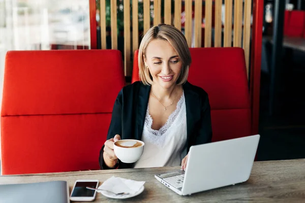 Retrato de uma jovem mulher bebendo café e usando um laptop em um café — Fotografia de Stock