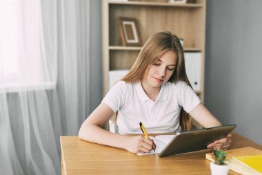 Çekici bir öğrenci çevrimiçi bir ders çalışıyor ve sınava bir tabletle hazırlanırken notlar alıyor. Eğitim ve terbiye kavramı, sınavlara hazırlık