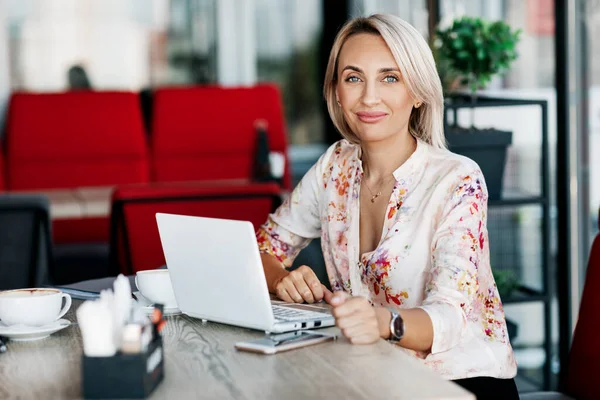 Uma linda garota trabalha on-line em um laptop, senta-se em um café ou escritório, usa uma conexão remota à Internet para o trabalho remoto. Freelance, negócios, negócios online — Fotografia de Stock