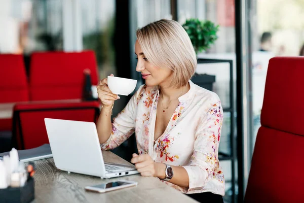 Uma mulher de negócios elegante bebe café, trabalha em um café, usa um laptop, desfruta de uma pausa. Negócios, negócios online, freelance — Fotografia de Stock