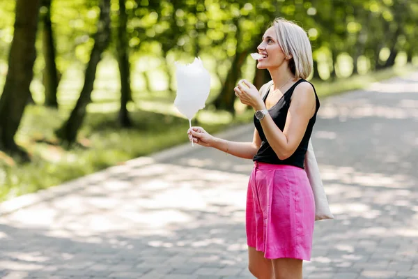 Mladá žena s cukrovou vatou kráčí uličkou v parku — Stock fotografie
