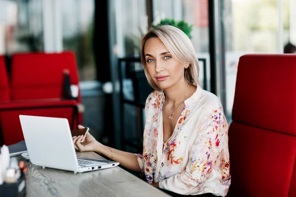 Uma linda garota trabalha on-line em um laptop, senta-se em um café ou escritório, usa uma conexão remota à Internet para o trabalho remoto. Freelance, negócios, negócios online — Fotografia de Stock