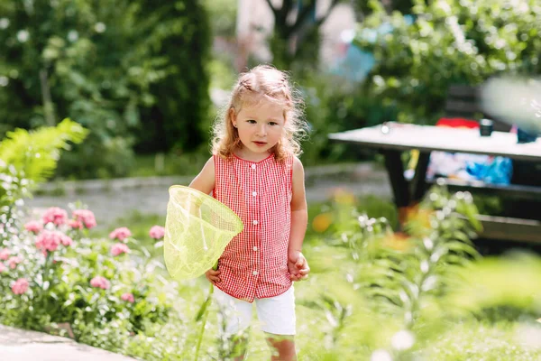 Маленька дівчинка з сіткою в руці грає в саду і ловить міль — стокове фото