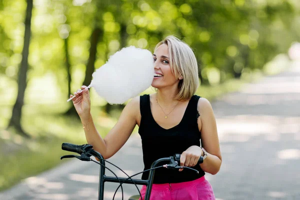 Retrato de uma linda garota loira com algodão doce em uma bicicleta. Descanso, fim de semana, hora de verão — Fotografia de Stock