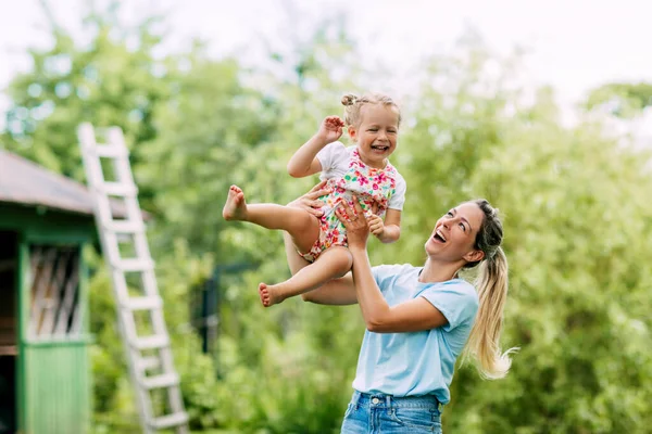 Een jonge moeder en haar schattige dochtertje hebben plezier in een zonnige tuin. Het concept van een gelukkige jeugd en moederschap, een moeder houdt haar dochtertje in haar armen — Stockfoto