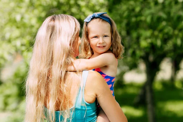 夏天的一天，一位年轻的母亲在花园里或公园里抱着她的小女儿 — 图库照片